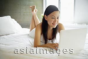Asia Images Group - Woman in bedroom, using laptop
