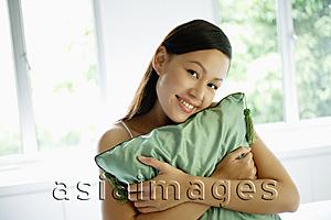 Asia Images Group - Woman hugging green cushion, smiling at camera