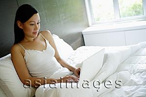 Asia Images Group - Woman sitting up in bed, using laptop
