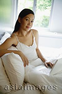 Asia Images Group - Woman on bed with laptop, looking at camera