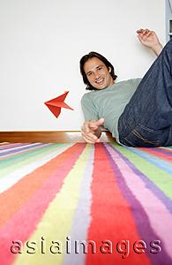 Asia Images Group - Man sitting on striped carpet, throwing paper airplane