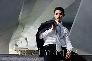 Asia Images Group - Businessman sitting on ledge, holding jacket over shoulder, looking at camera