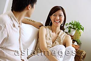 Asia Images Group - Couple sitting on sofa, woman hugging knees, smiling at man