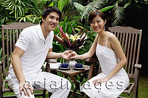 Asia Images Group - Couple sitting in garden, holding hands, smiling at camera