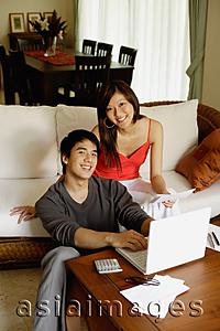 Asia Images Group - Couple in living room, using laptop, looking at camera