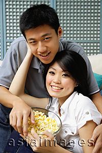 Asia Images Group - Couple with bowl of popcorn, looking at camera