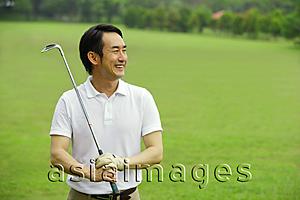 Asia Images Group - Man holding golf club, smiling, looking away