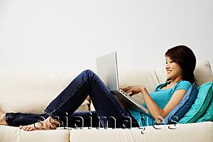 Asia Images Group - Woman lying on sofa, using laptop