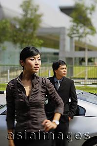 Asia Images Group - Businessman leaning on car, woman in foreground, with hand on hip