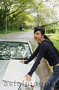 Asia Images Group - Woman with map spread out on hood of car, looking at camera