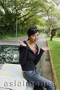 Asia Images Group - Woman sitting on hood of car, map next to her, hands raised