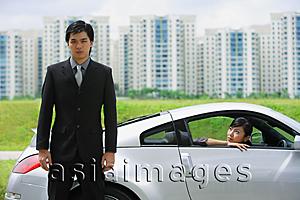Asia Images Group - Businessman standing next to sports car, woman in car, looking out the car window