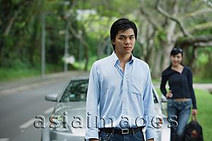 Asia Images Group - Man standing in front of car, woman in the background with luggage