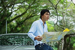 Asia Images Group - Man sitting on hood of car, holding map, looking away