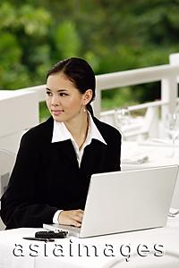 Asia Images Group - Businesswoman with laptop, sitting in restaurant, looking away