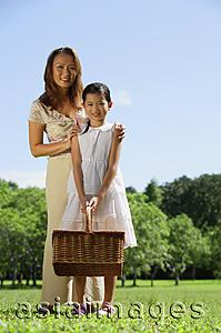 Asia Images Group - Mother and daughter in park, looking at camera, girl holding picnic basket