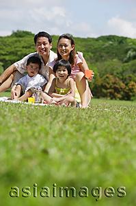 Asia Images Group - Family of four sitting on picnic mat, looking at camera