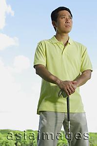 Asia Images Group - Man standing, leaning on golf club, looking away