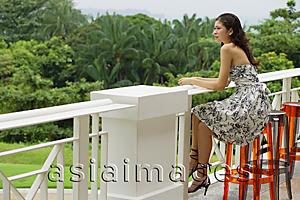 Asia Images Group - Young woman sitting on bar stool, leaning on railing