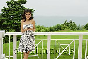 Asia Images Group - Young woman in floral dress, standing on balcony, holding mobile phone