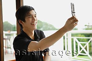 Asia Images Group - Man in cafe using mobile phone to take a picture of himself