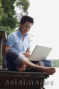 Asia Images Group - Man sitting on jetty, using laptop