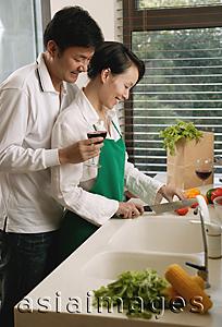 Asia Images Group - Couple in kitchen, woman chopping vegetables, man standing next to her, holding wine glass