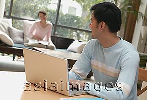 Asia Images Group - Man using laptop turning to look at woman in background