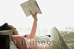 Asia Images Group - Woman lying on sofa, reading a book
