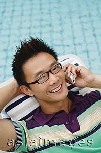 Asia Images Group - Man using mobile phone, smiling, swimming pool in the background