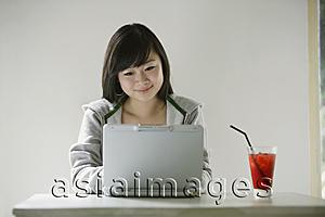 Asia Images Group - Young woman using laptop, drink on table next to her