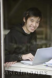 Asia Images Group - Young man using laptop, smiling at camera