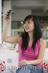 Asia Images Group - Young woman holding mobile phone, taking a picture of herself