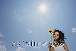 Asia Images Group - Woman holding sunflower stalk, smiling at camera, low angle view