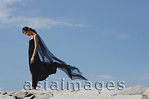 Asia Images Group - Woman in black dress and scarf, standing on rocks, looking down