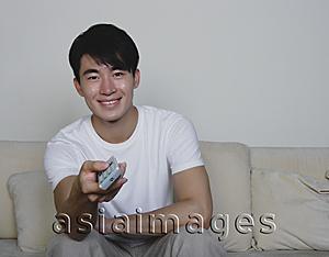 Asia Images Group - Young man holding TV remote control, smiling