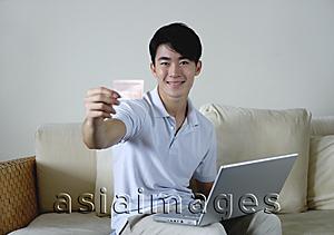 Asia Images Group - Man sitting on sofa with laptop, holding out credit card