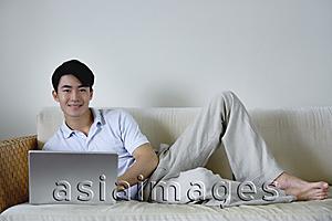 Asia Images Group - Man lying on sofa with laptop