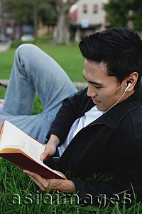 Asia Images Group - College student lying on grass, reading a book