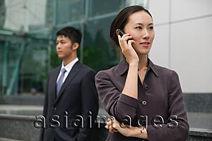 Asia Images Group - Businesswoman on mobile phone, man in the background