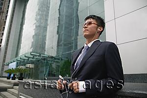 Asia Images Group - Businessman in city location, listening to MP3 player