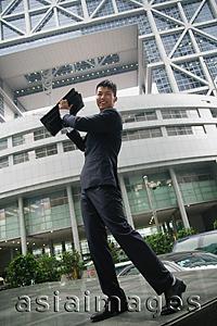 Asia Images Group - Businessman lifting briefcase in air, smiling at camera