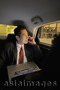 Asia Images Group - Mature man sitting in back seat of the car with a laptop and phone