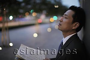 Asia Images Group - Mature man leaning against a wall with eyes closed in the evening.