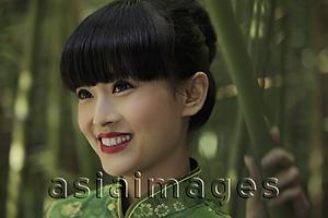 Asia Images Group - Head shot of young woman wearing a traditional Chinese dress and standing in front of bamboo trees.