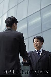Asia Images Group - Businessmen shaking hands in front of a building