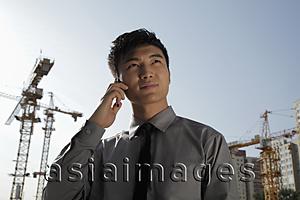 Asia Images Group - young man holding phone standing in front of construction site