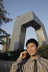 Asia Images Group - Young man talking on phone in front of CCTV Building