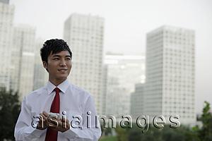 Asia Images Group - Young man texting on phone with buildings as background