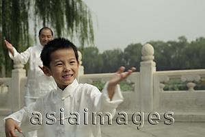 Asia Images Group - Young boy doing Tai Chi with older man in background